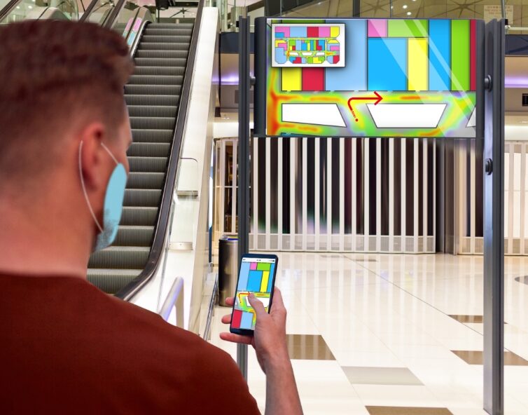 Visitatore con mascherina che consulta la mappa 4Safe sullo smartphone davanti a un totem d’ingresso in un centro commerciale